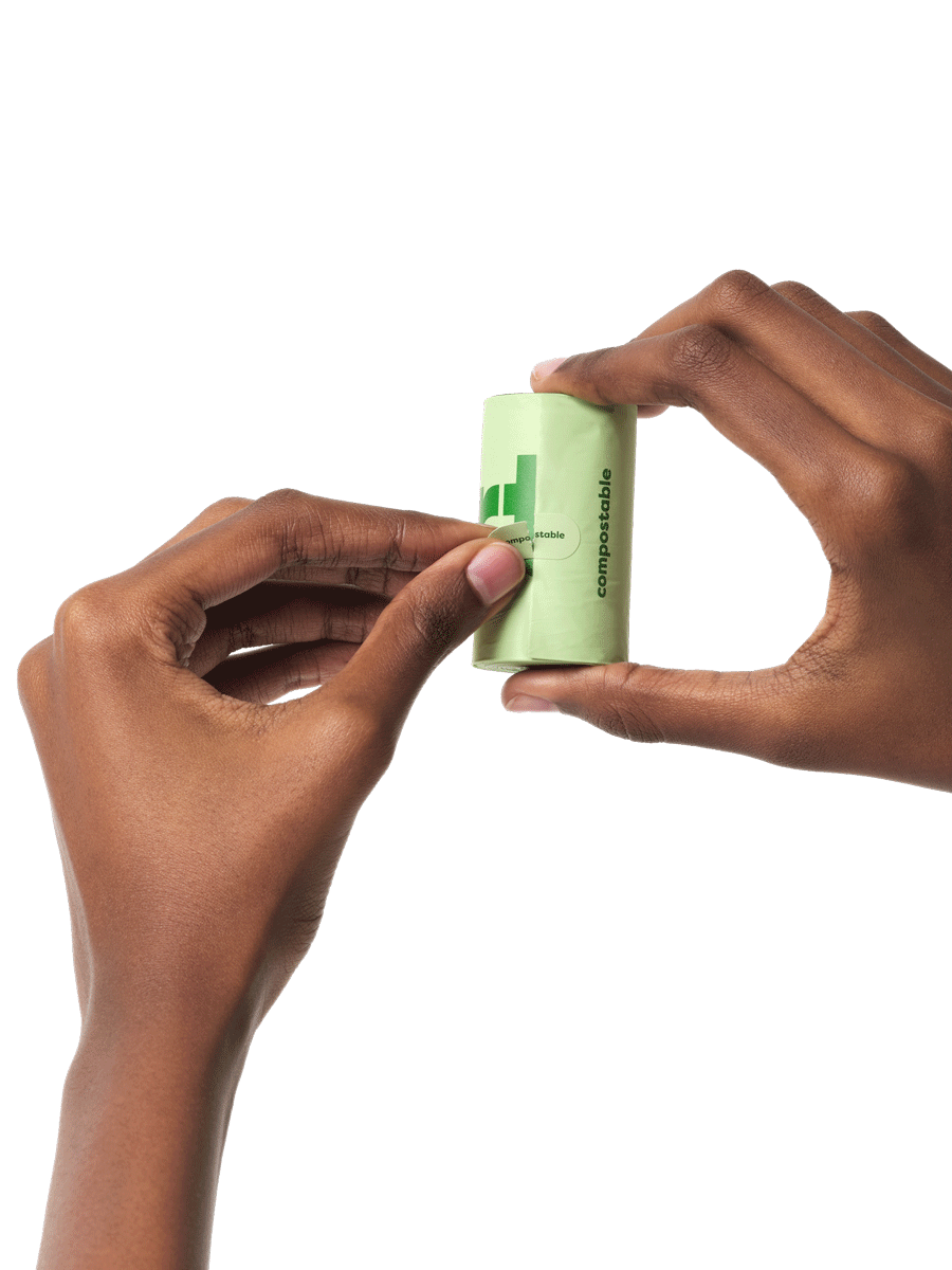 Hands holding a roll of compostable dog poop bags and tearing off a perforated sticker